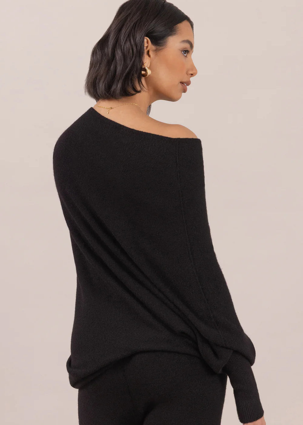 Woman wearing a black off-shoulder top and pants on a beige background