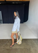 Woman in a light blue shirt and beige shorts holding a yellow and white bag in an indoor setting.