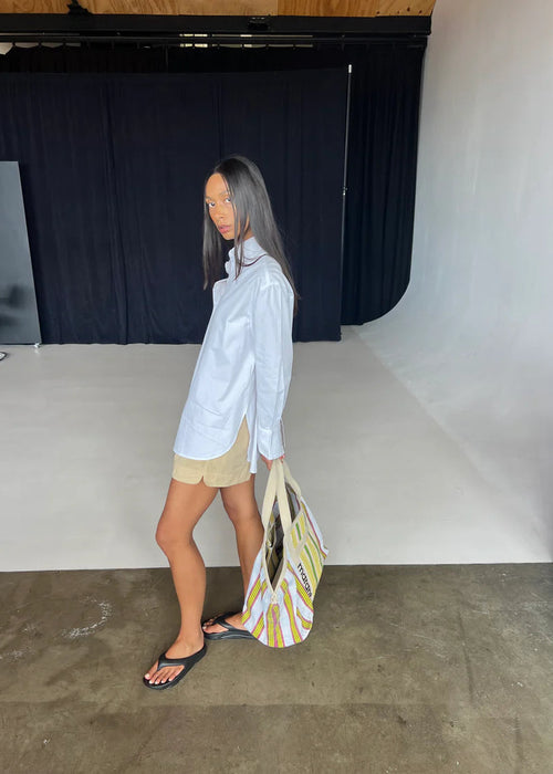 Woman in a light blue shirt and beige shorts holding a yellow and white bag in an indoor setting.