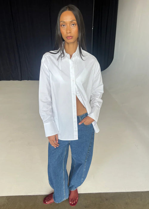 Person wearing a white shirt and blue jeans against a plain background