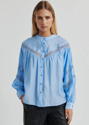 Woman wearing a light blue blouse with intricate patterns on a plain background