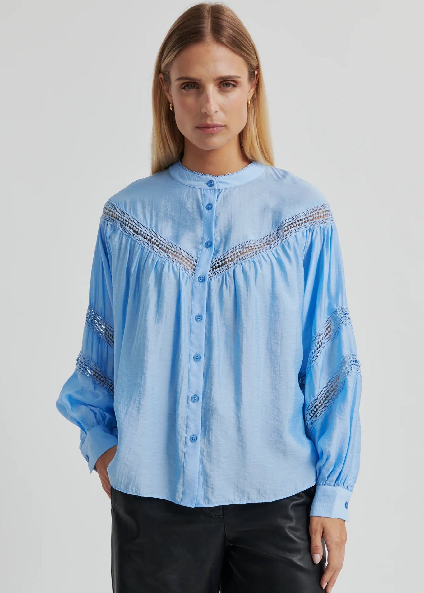 Woman wearing a light blue blouse with intricate patterns on a plain background