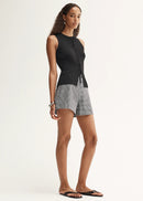 Woman wearing a black sleeveless top and grey checkered shorts on a white background