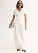 Woman wearing a white outfit with sunglasses and holding a patterned clutch against a white background