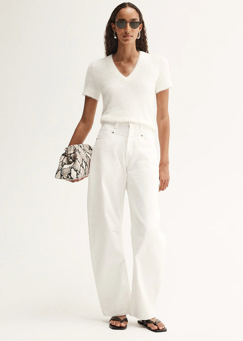 Woman wearing a white outfit with sunglasses and holding a patterned clutch against a white background