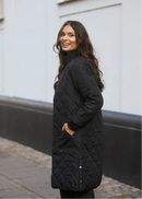 Woman in black coat and pants standing on a street with a white building in the background