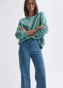 Woman wearing a teal sweater and blue jeans on a white background