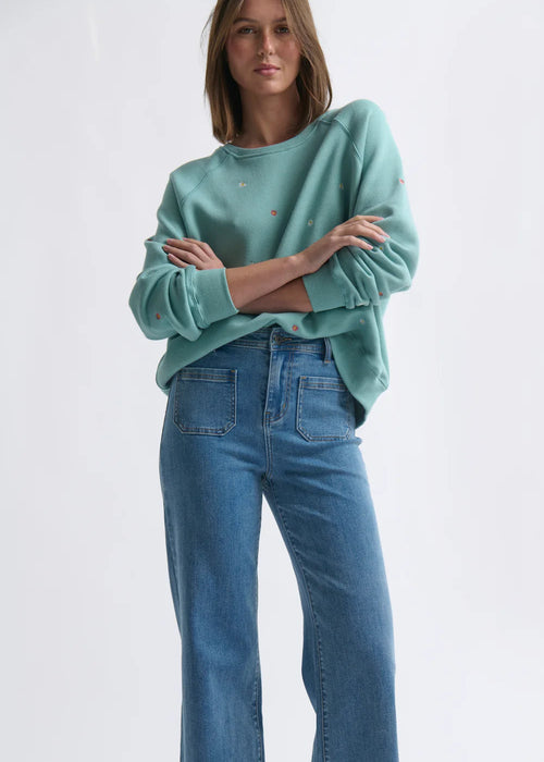 Woman wearing a teal sweater and blue jeans on a white background