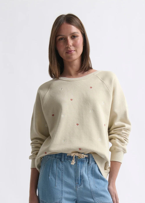 Woman wearing a beige sweater with small red patterns and blue jeans on a white background