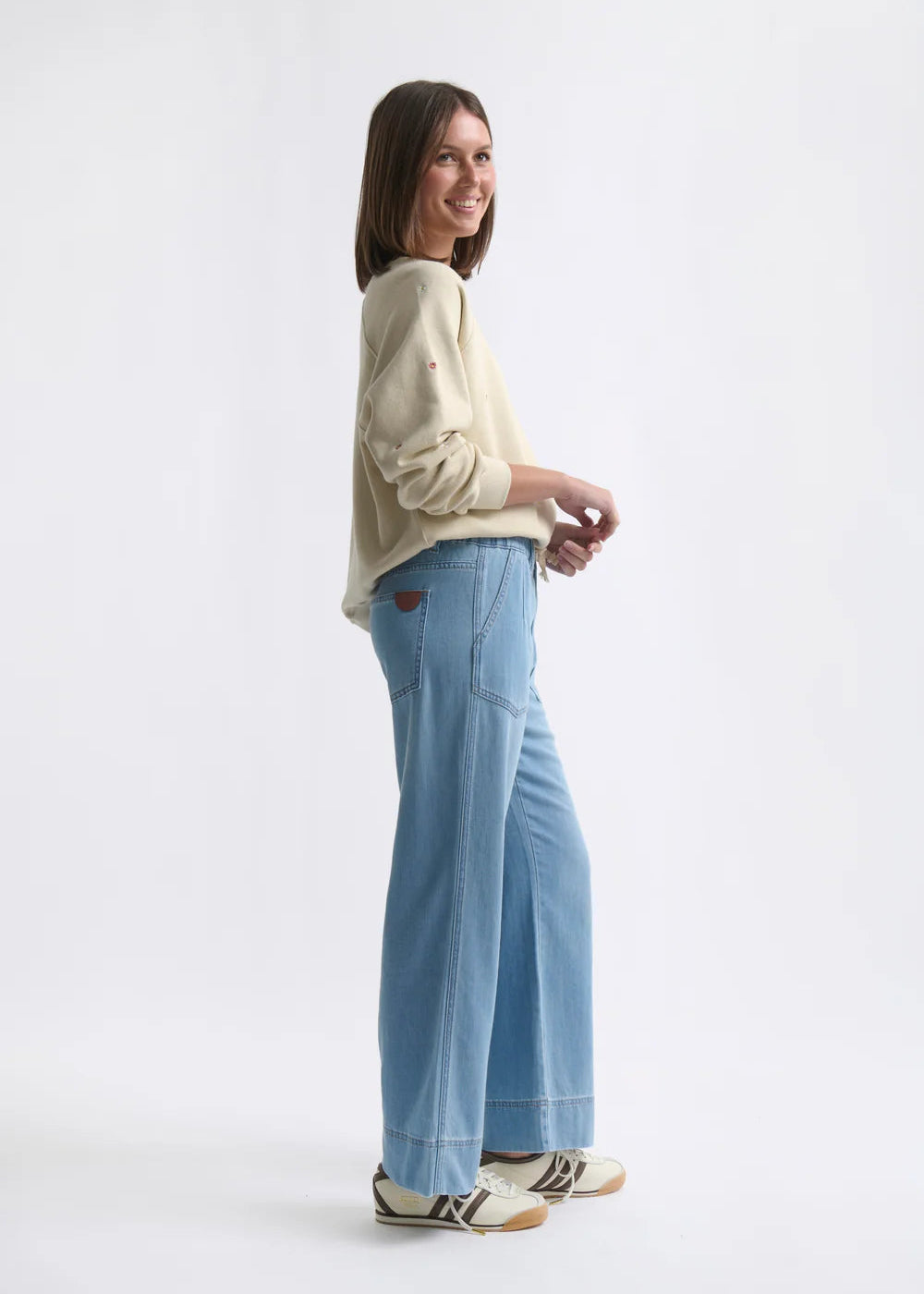 Woman wearing a light-coloured sweater and blue pants on a white background