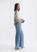 Woman wearing a light-coloured sweater and blue pants on a white background