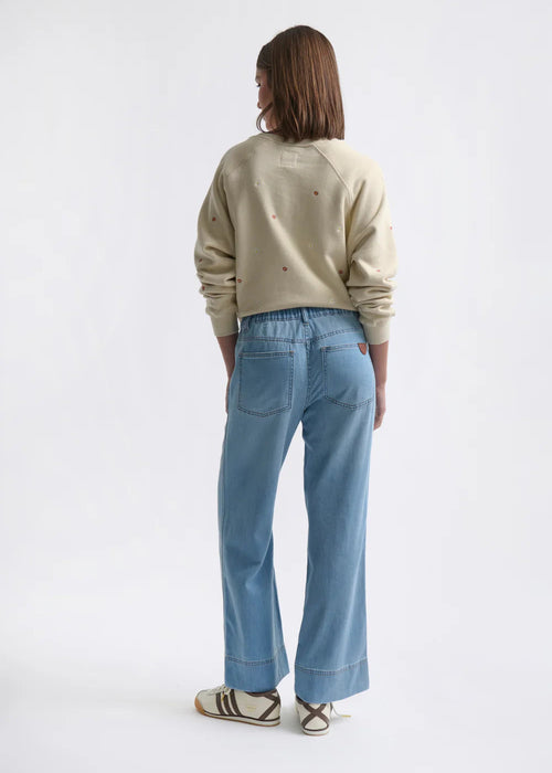 Person wearing a beige sweater and light blue jeans on a white background