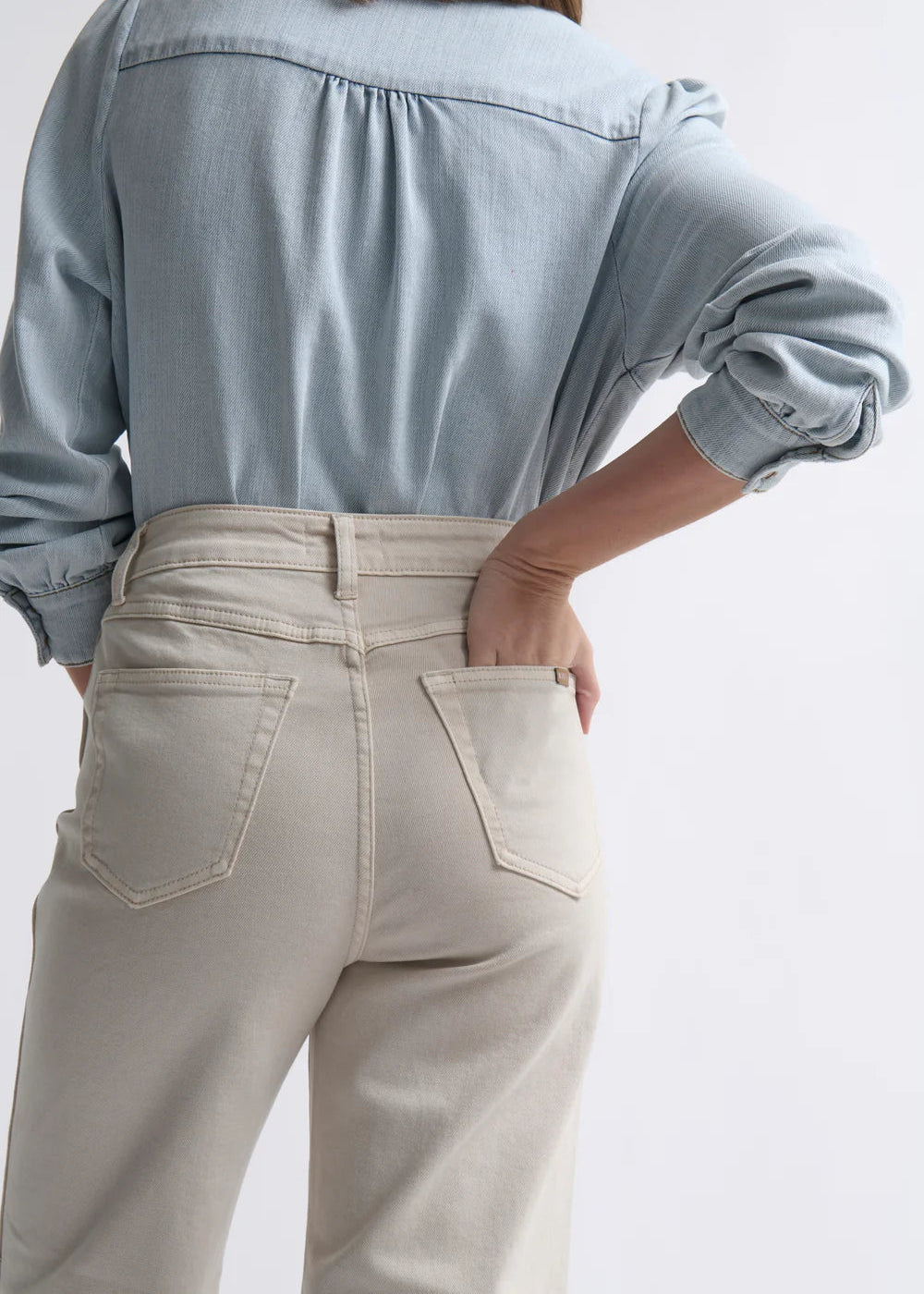 Woman wearing a light blue shirt and beige pants on a white background