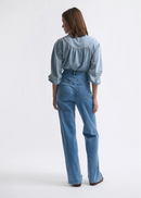 Person wearing a light blue denim shirt and jeans on a white background