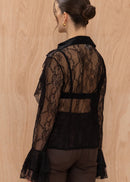 Woman wearing a black lace top and brown pants against a wooden background