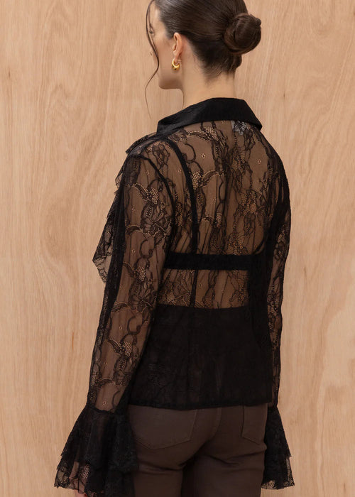 Woman wearing a black lace top and brown pants against a wooden background
