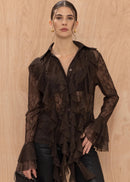 Woman wearing a sheer brown blouse with ruffled layers against a beige background