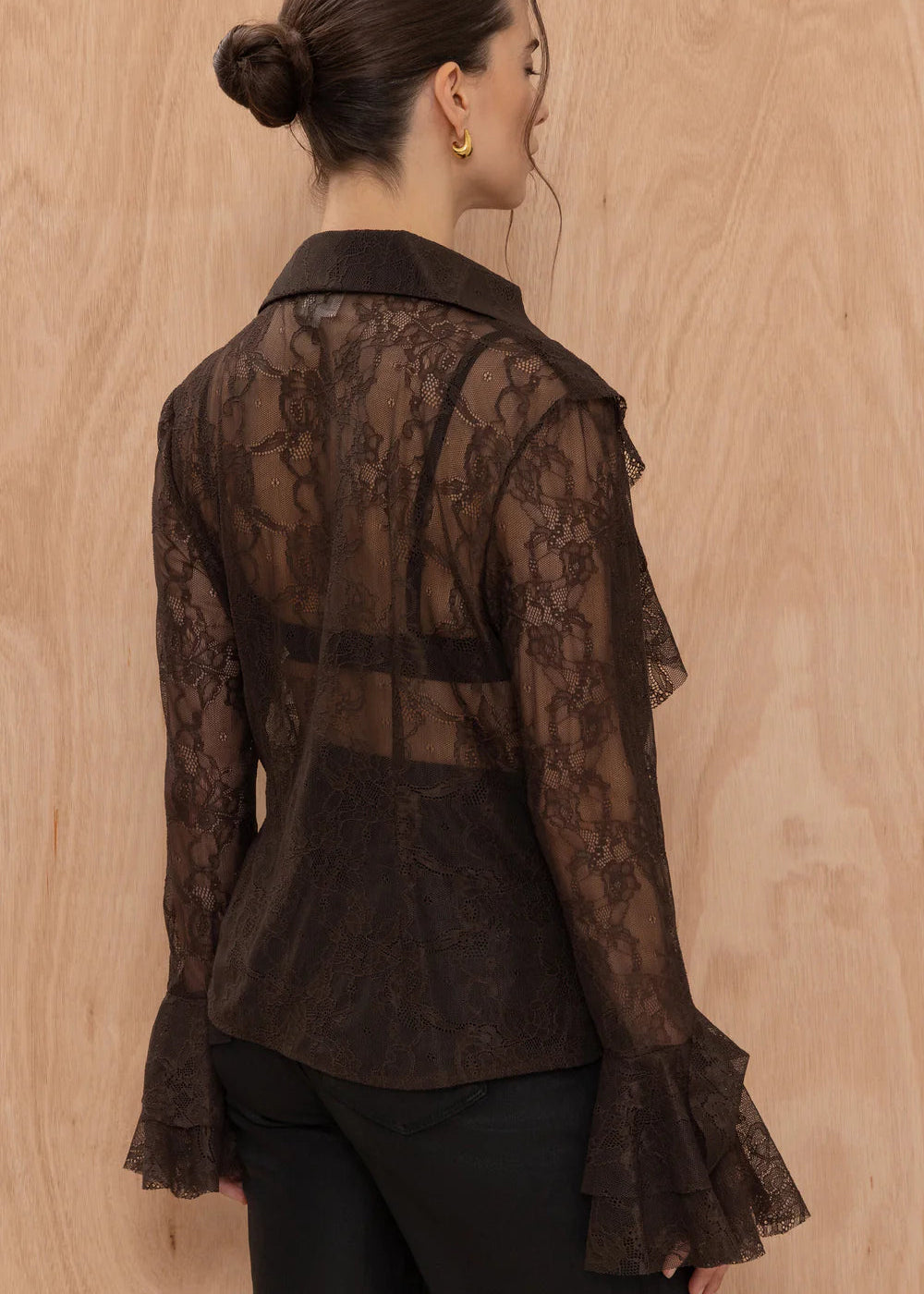 Woman wearing a sheer brown lace blouse against a wooden background