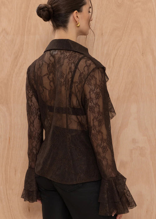Woman wearing a sheer brown lace blouse against a wooden background