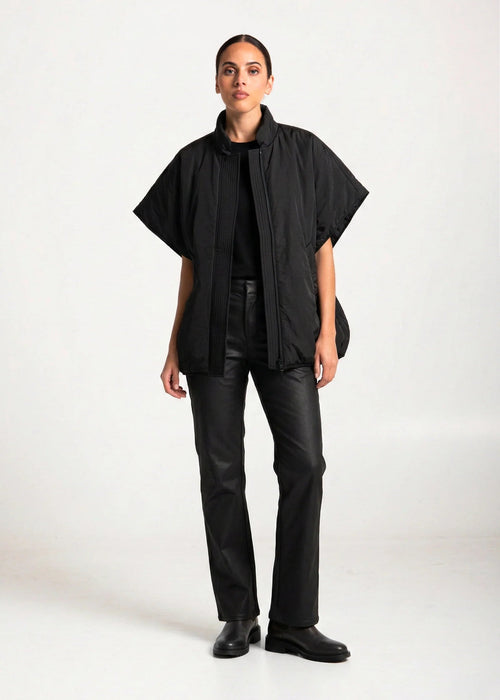 Person wearing a black poncho over a black top and pants on a white background