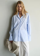 Woman wearing a light blue striped shirt against a plain background