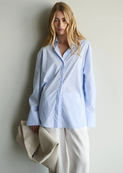 Woman wearing a light blue striped shirt against a plain background
