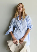 Woman wearing a light blue shirt holding a beige clutch against a plain background