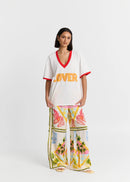 Woman wearing a white top with 'LOVER' text and colourful pants on a white background