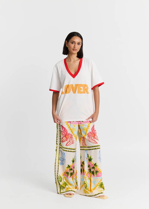 Woman wearing a white top with 'LOVER' text and colourful pants on a white background