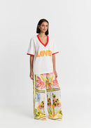 Woman wearing a white 'LOVE' top with red trim and colourful pants on a white background