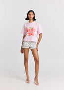 Woman wearing a pink 'Sweetie' t-shirt and patterned shorts on a white background