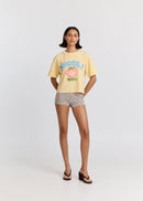 Woman wearing a yellow t-shirt with a graphic design and checkered shorts on a white background