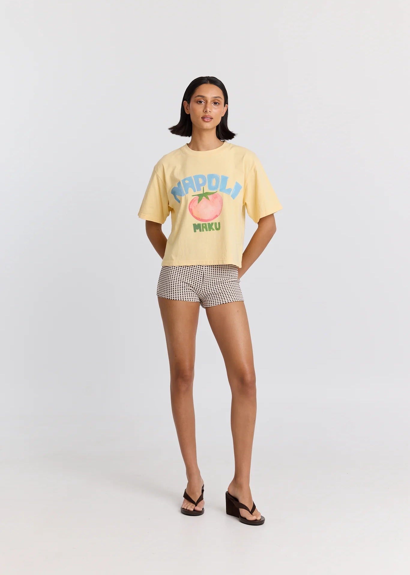 Woman wearing a yellow t-shirt with a graphic design and checkered shorts on a white background