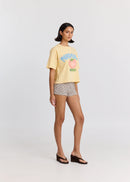 Woman wearing a yellow t-shirt with text and graphics, checkered shorts, and sandals on a white background