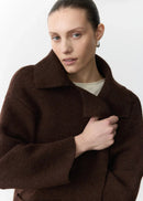 Woman wearing a brown coat and blue pants holding a chair against a white background