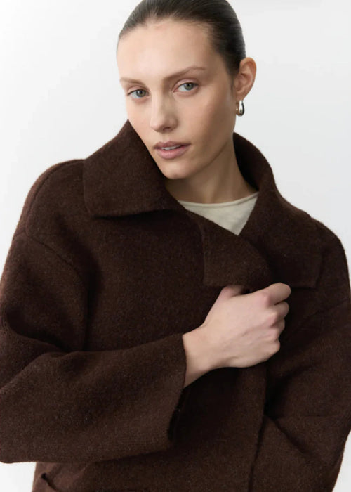 Woman wearing a brown coat and blue pants holding a chair against a white background