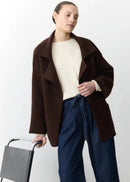Woman wearing a brown coat and blue pants holding a chair against a white background