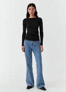 Woman wearing a black long-sleeve top and blue jeans on a white background