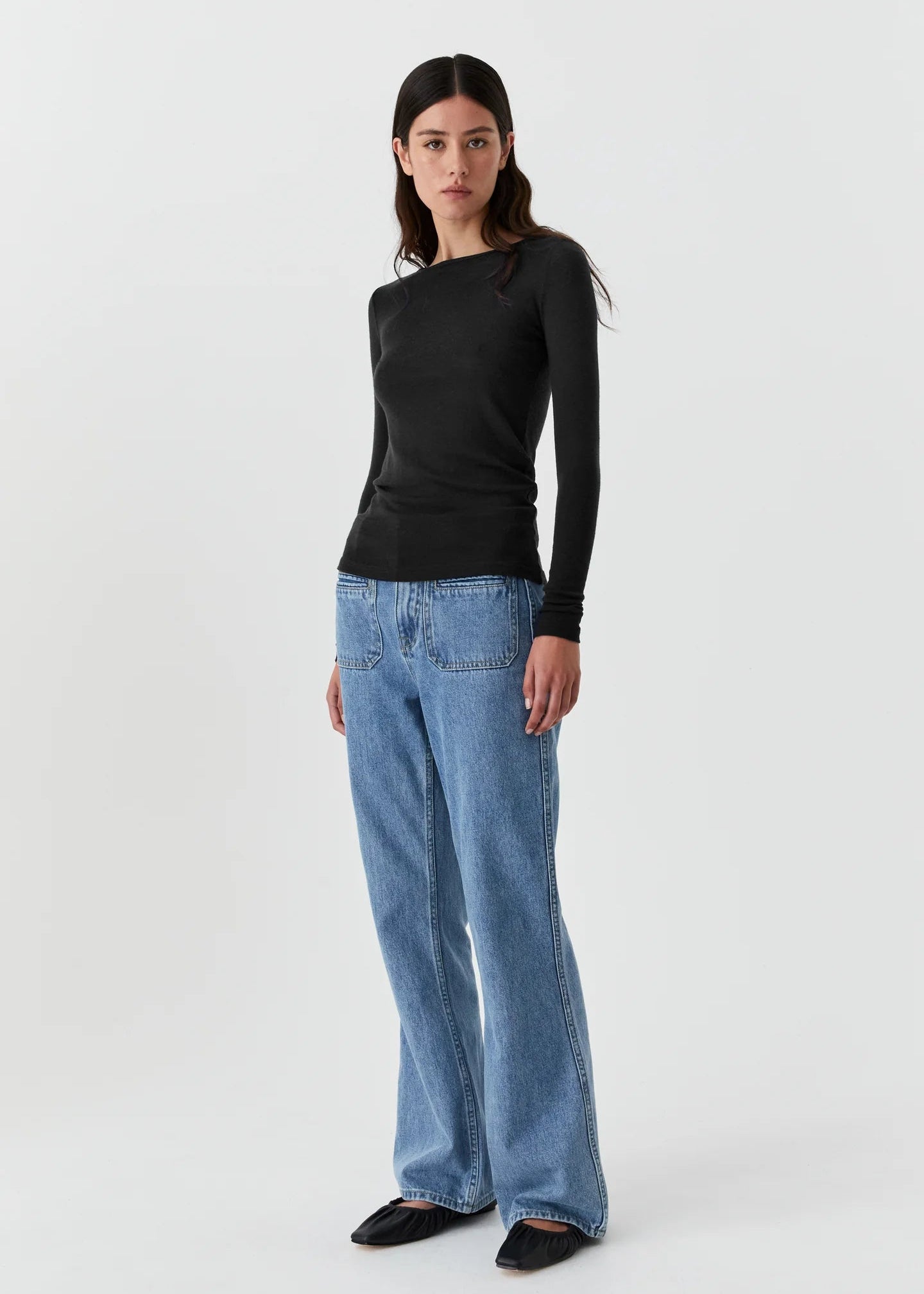 Woman wearing a black top and blue jeans on a white background