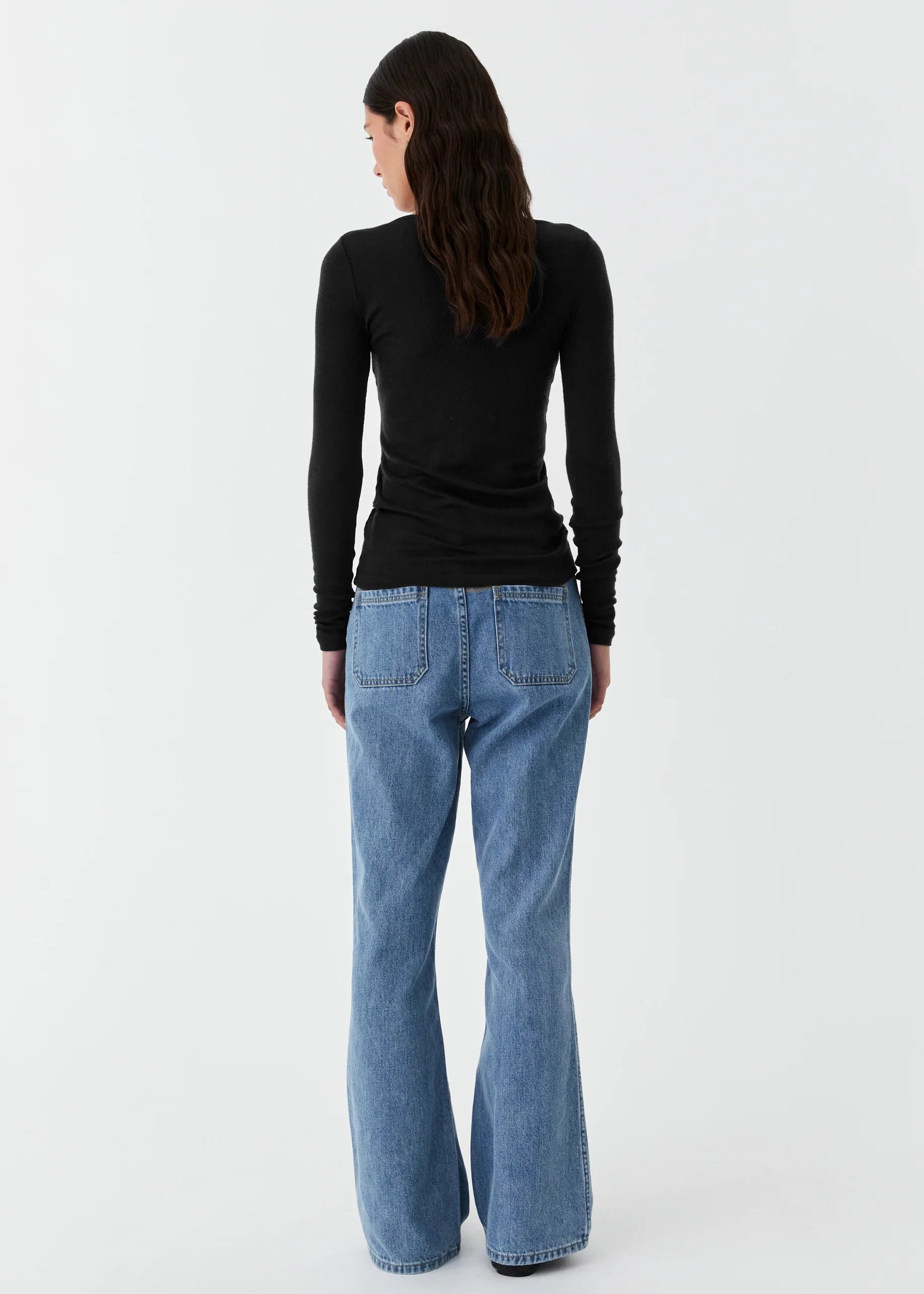 Person wearing blue jeans and a black long-sleeve shirt on a white background