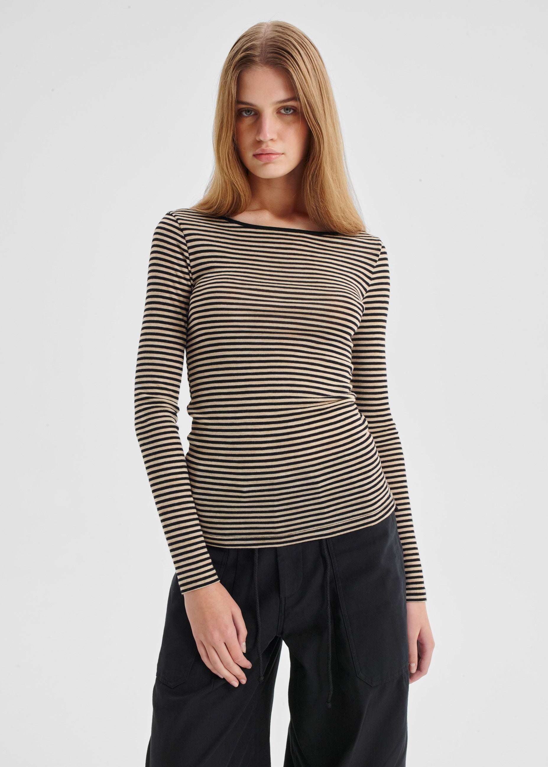 Woman wearing a striped long-sleeve top and black pants on a light gray background