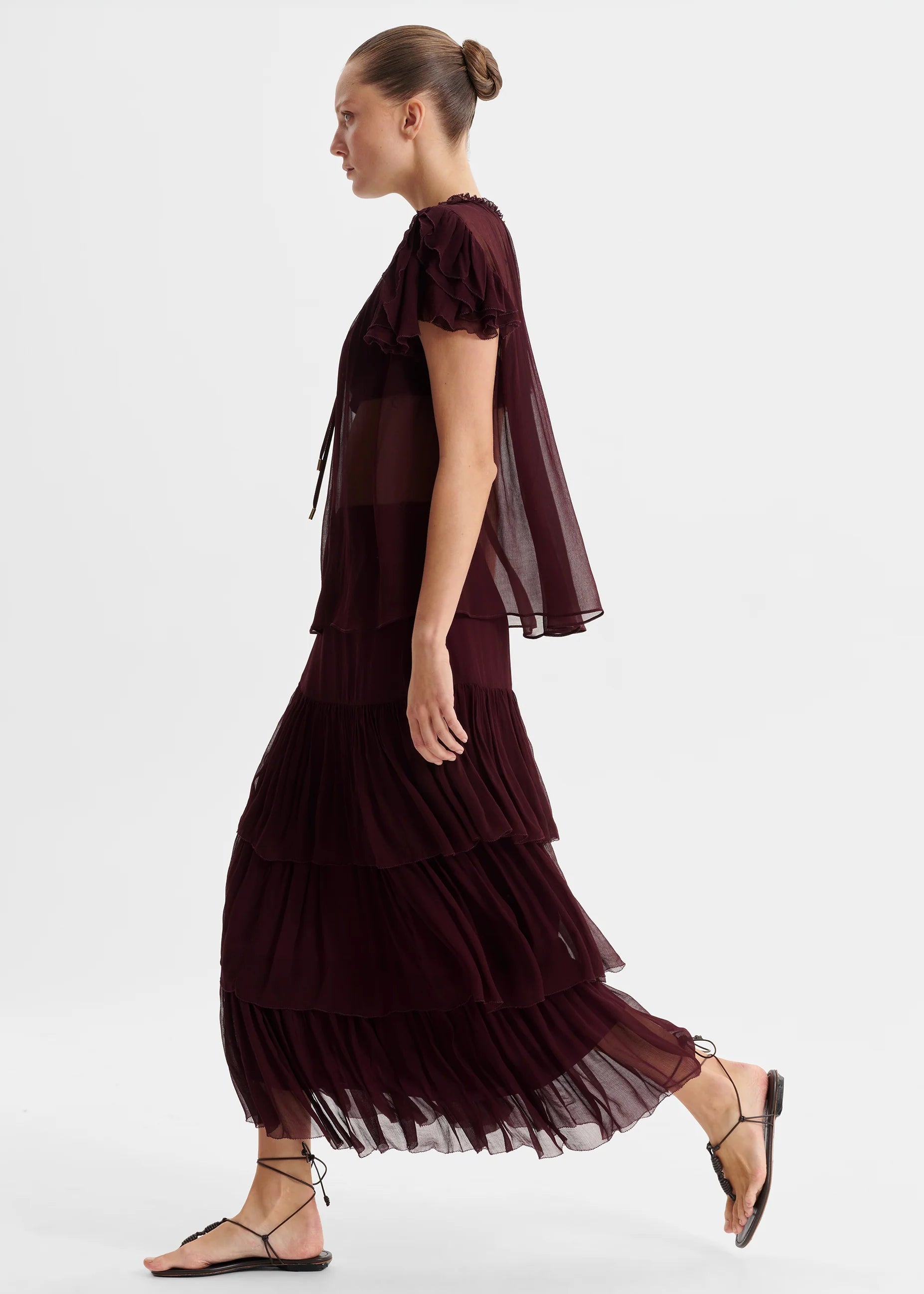 Woman wearing a burgundy dress with sheer overlay on a white background