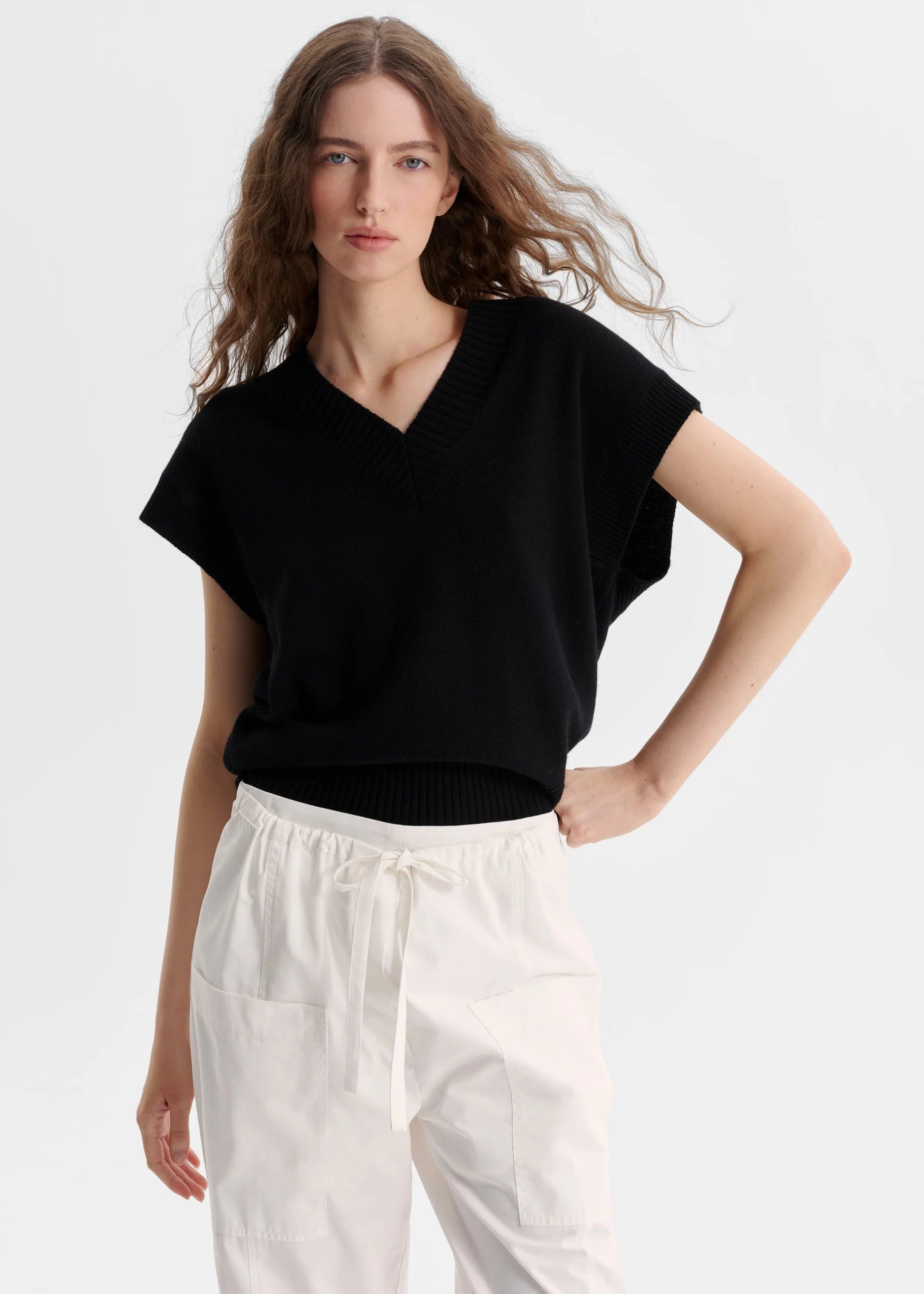 Woman wearing a black top and white pants on a light grey background