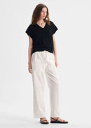 Woman wearing a black top and white pants on a white background