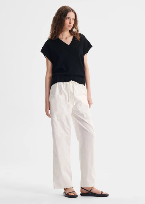Woman wearing a black top and white pants on a white background