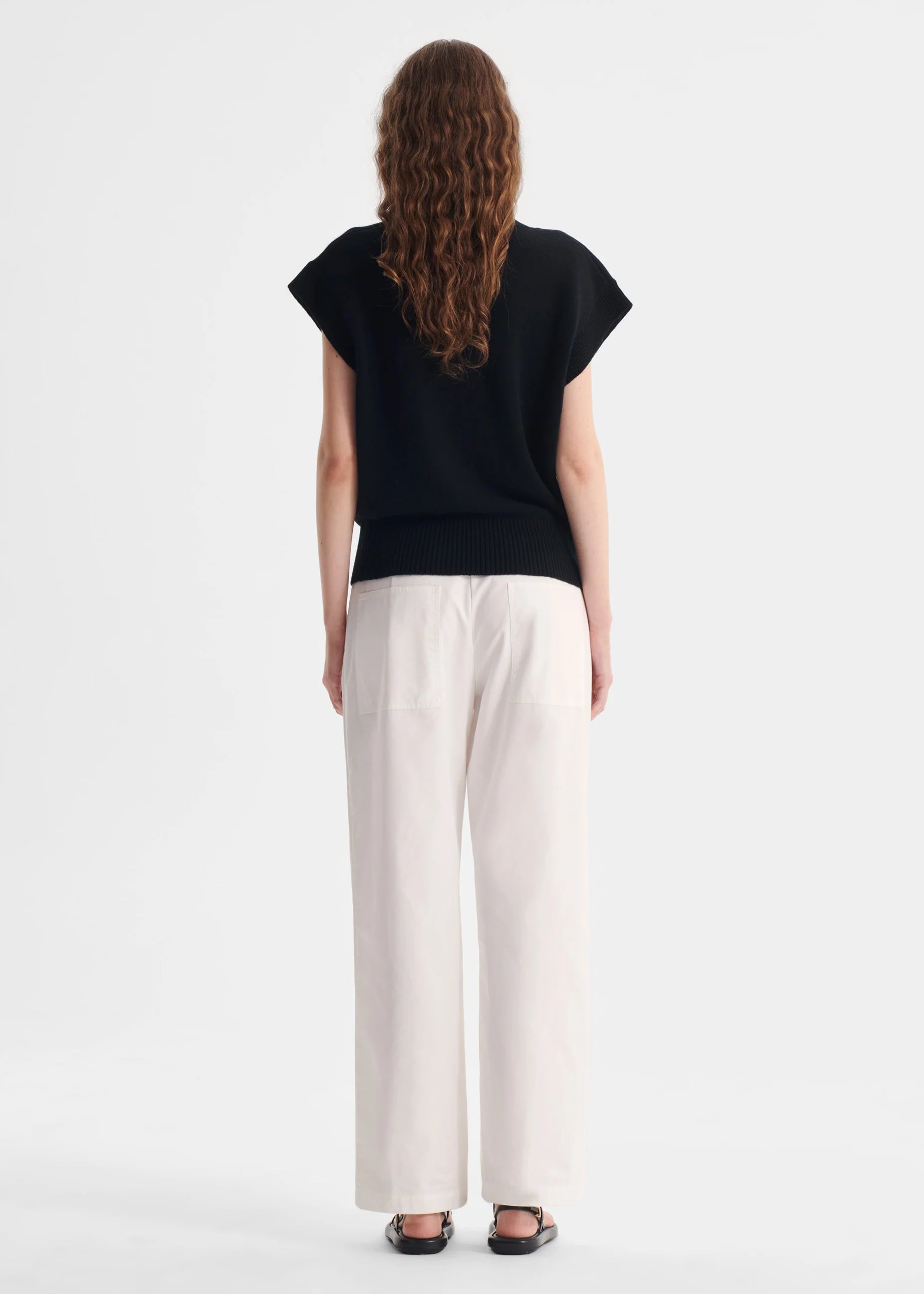 Person wearing a black top and white pants on a white background