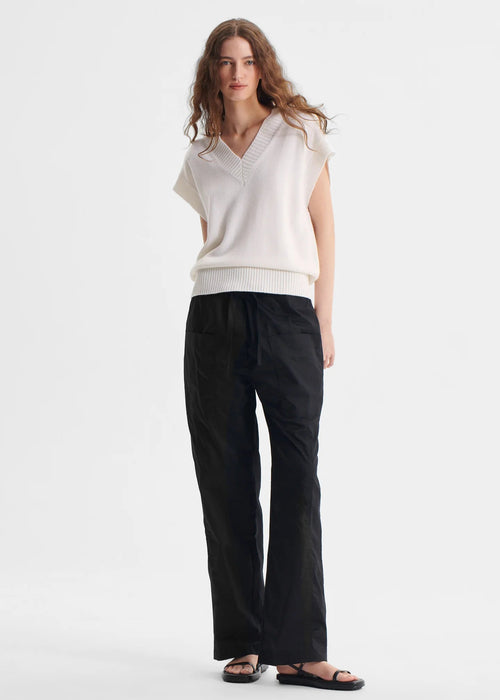 Woman wearing a white sleeveless top and black pants on a white background