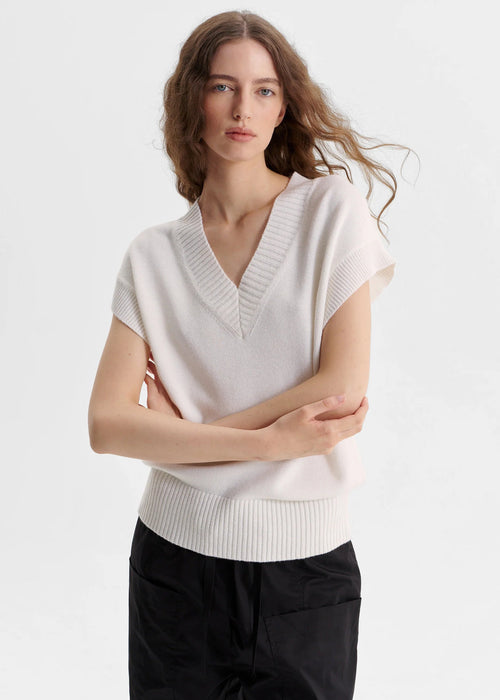 Woman wearing a white sweater with black pants on a light grey background