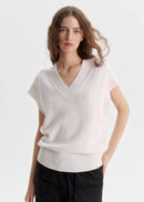 Woman wearing a white sleeveless sweater on a light grey background
