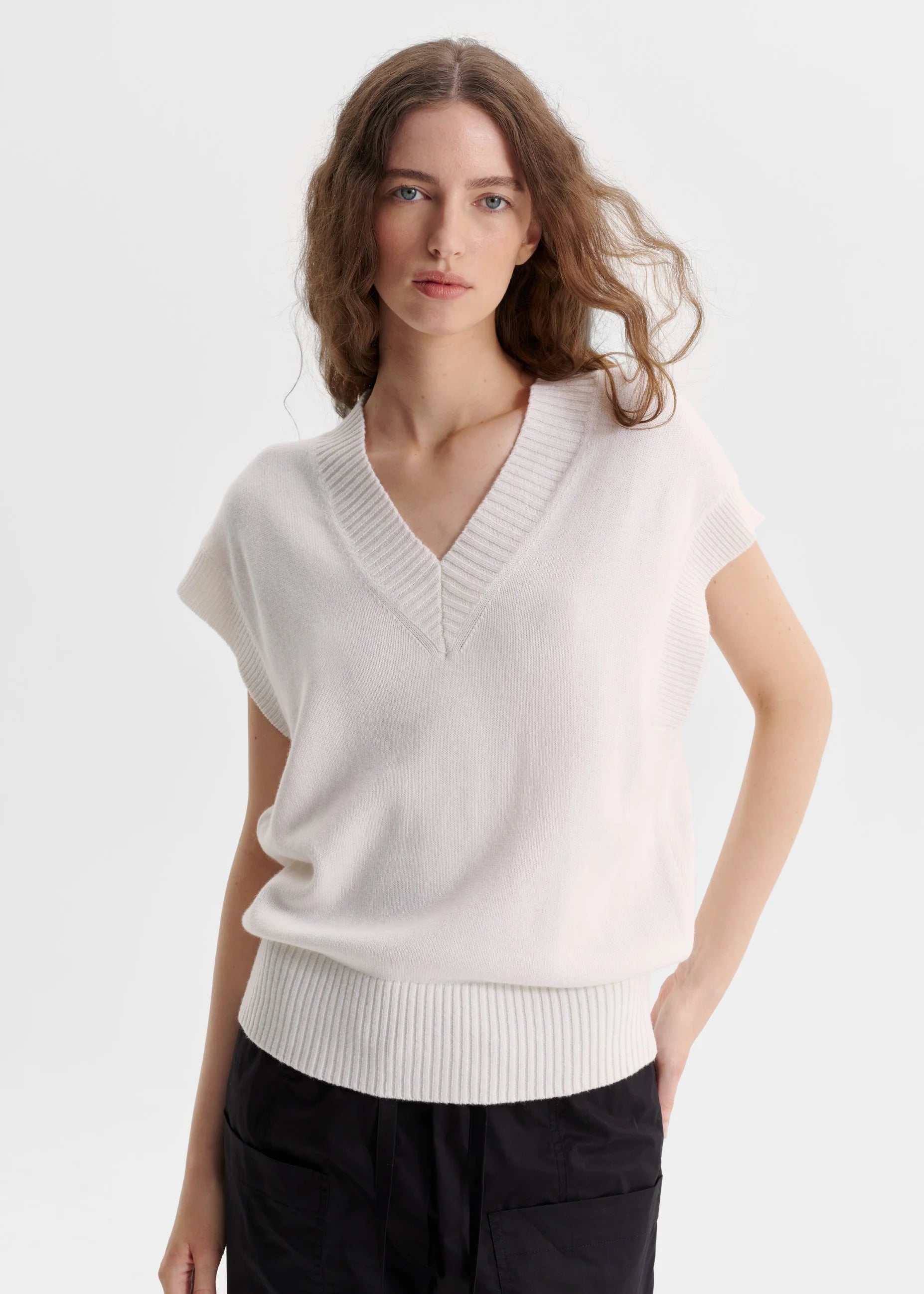Woman wearing a white sleeveless sweater on a light grey background